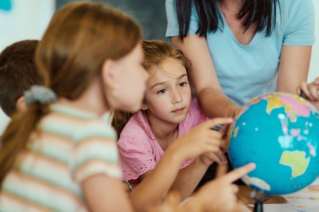 Niñas estudiando con su profesora sobre un mapamundi