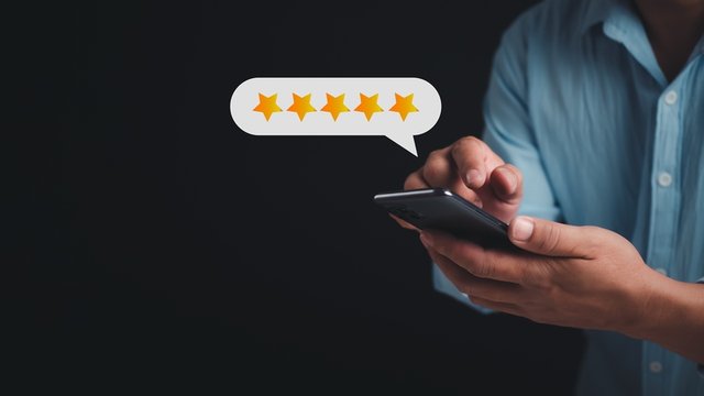 Las manos de una persona con un móvil colocando reseña de cinco estrellas expresado en pop up