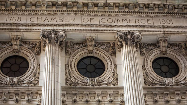 Architectural detail of a historic stone building facade featuring an engraved inscription above ornate columns and circular windows with decorative carvings.