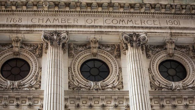 Architectural detail of a historic stone building facade featuring an engraved inscription above ornate columns and circular windows with decorative carvings.