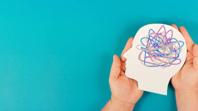 An image of two hands gently holding a white paper cutout of a human head profile on a bright blue background.