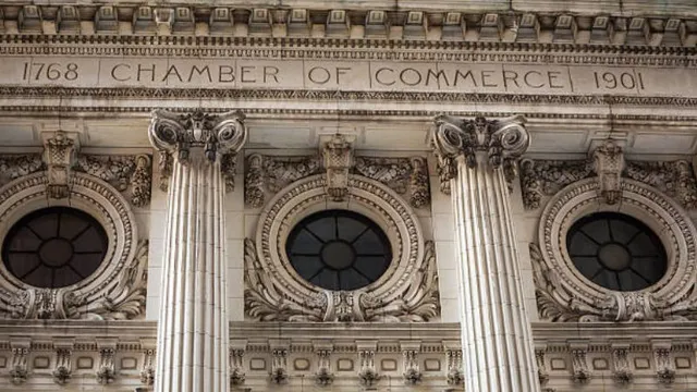 Architectural detail of a historic stone building facade featuring an engraved inscription above ornate columns and circular windows with decorative carvings.