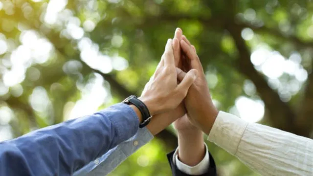 A group of people joining hands together in a high-five gesture outdoors, symbolizing unity, collaboration, and sports diplomacy against a blurred green park background.