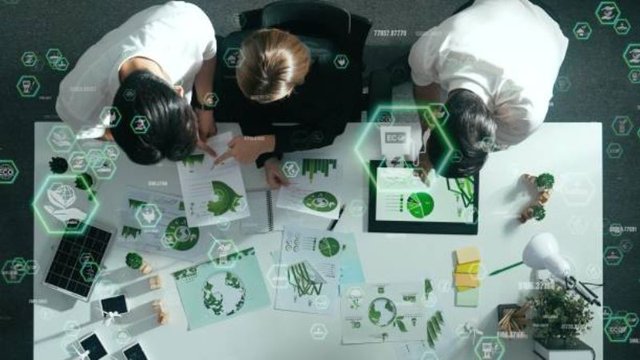 Top-down view of three team members working around a table with green charts, eco-friendly data graphics, and digital sustainability icons to plan sports sustainability initiatives.