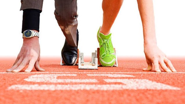 Close-up on starting blocks with a split focus: one leg in a business suit and dress shoe, the other bare with a neon running sneaker, illustrating the duality of an athlete representative.