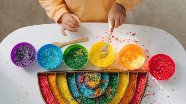 un niño juega con arroz de colores rellenando la figura de un arco iris