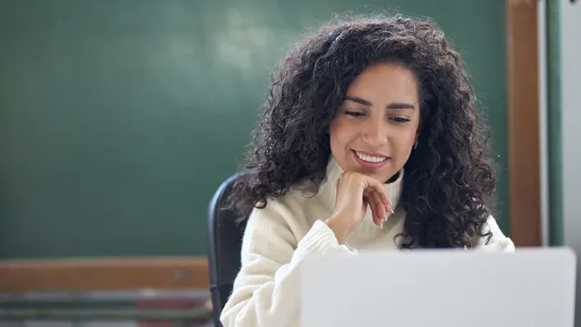 profesora sonriente usando un ordenador portátil en un aula