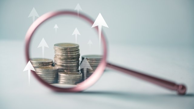 se utiliza una lupa para mirar una pila de monedas. Las monedas están apiladas en forma de pirámide