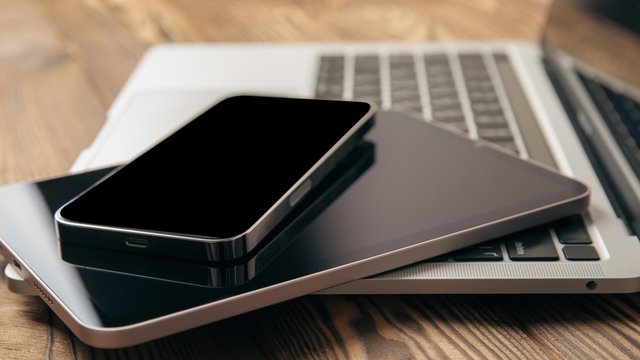 ordenador portátil puesto sobre una mesa de madera, junto con una tablet y un teléfono móvil