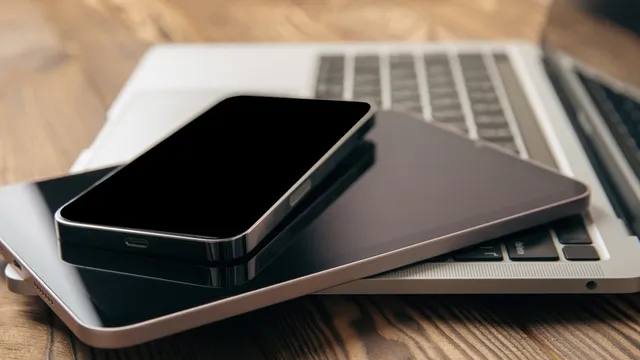 ordenador portátil puesto sobre una mesa de madera, junto con una tablet y un teléfono móvil