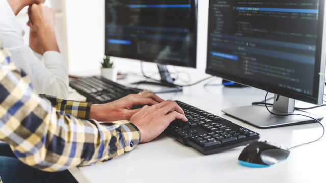 dos personas trabajan en el c&oacute;digo de un programa de software con dos monitores