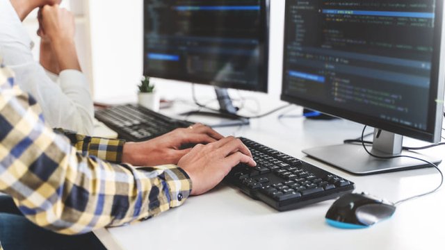 dos personas trabajan en el código de un programa de software con dos monitores