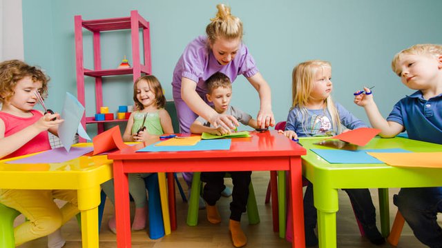 educadora infantil ayuda a unos estudiantes a realizar una actividad