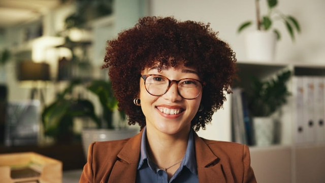 primer plano de una chica de pelo rizado y con gafas mirando sonriente a cámara