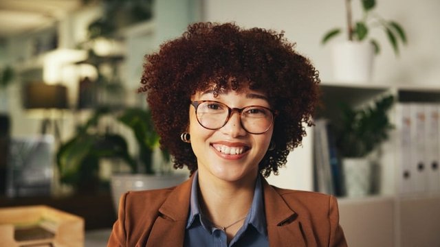 primer plano de una chica de pelo rizado y con gafas mirando sonriente a cámara