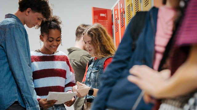 Estudiantes adolescentes pasando el rato en el pasillo de la escuela por taquillas, mirando el proyecto.