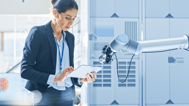 mujer ingeniera usa una tablet para programar un brazo robótico