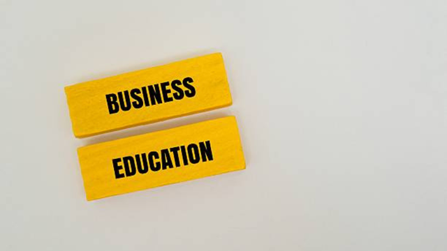 Two yellow wooden blocks placed parallel to each other on a white background, with the words "BUSINESS" and "EDUCATION" printed on them in black capital letters.