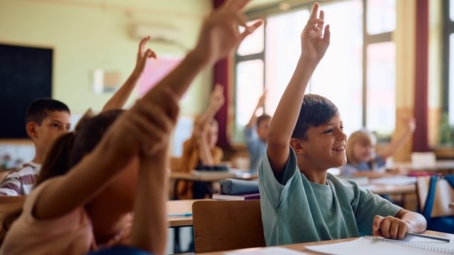 estudiantes de primaria en el aula levantando el brazo para responder a la pregunta de la maestra
