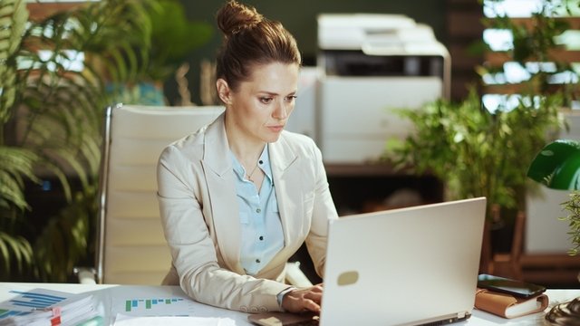 trabajadora vestida de traje usando un ordenador portátil en una oficina moderna y verde