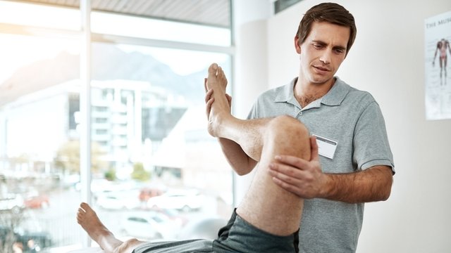 fisioterapeuta realiza ejercicios de rehabilitación de pierna en un consultorio