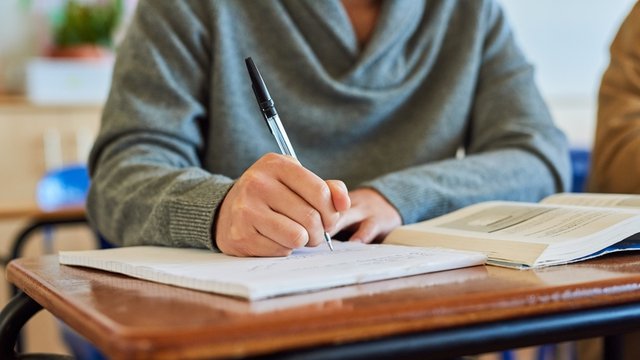 estudiante universitario toma apuntes en una libreta, mientras lee un libro