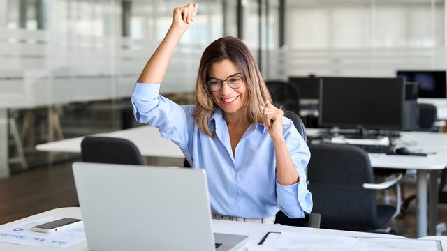 chica de mediana edad contenta en una oficina al mirar la pantalla de su ordenador portátil