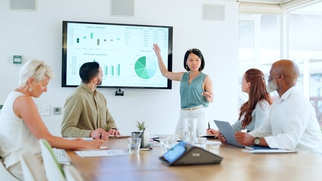 personas sentadas alrededor de una mesa de trabajo, mientras chica hace una exposición