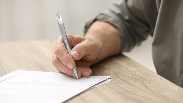persona adulta firma un testamento con bol&iacute;grafo sobre una mesa de madera