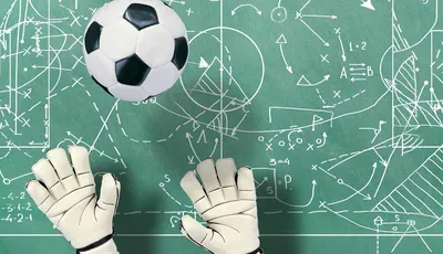 guantes de portero de fútbol y balón de fútbol sobre fondo de pizarra verde con estrategias de campo dibujadas