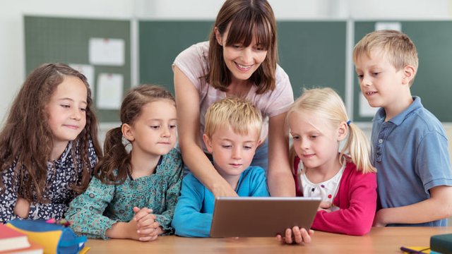 maestra enseñando a unos estudiantes a usar una tablet en el aula