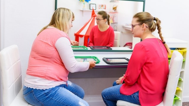 docente enseñando a una madre a usar un dispositivo de comunicación aumentativa y alternativa (caa)