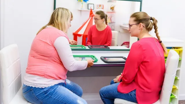 docente enseñando a una madre a usar un dispositivo de comunicación aumentativa y alternativa (caa)