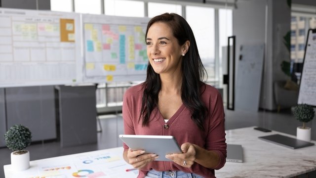 mujer profesional feliz de pie en la oficina, sostiene una tableta y mira al infinito