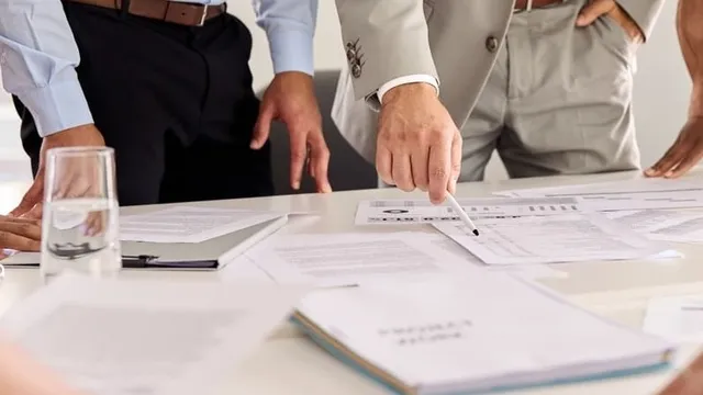 varios hombres reunidos alrededor de unos documentos que hay sobre una mesa de color claro