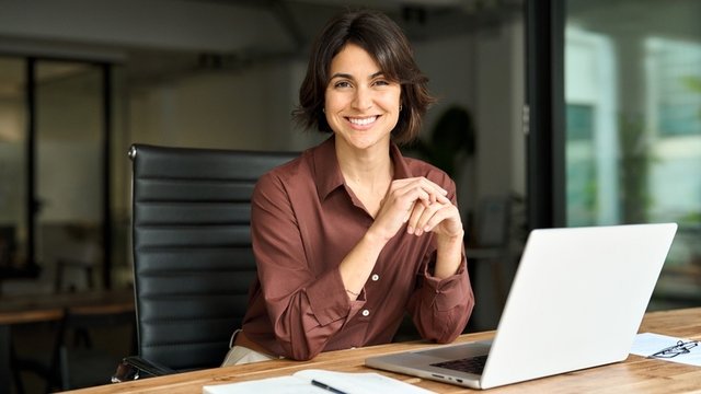 directora de banco sonriente, sentada y con los codos apoyados sobre el escritorio