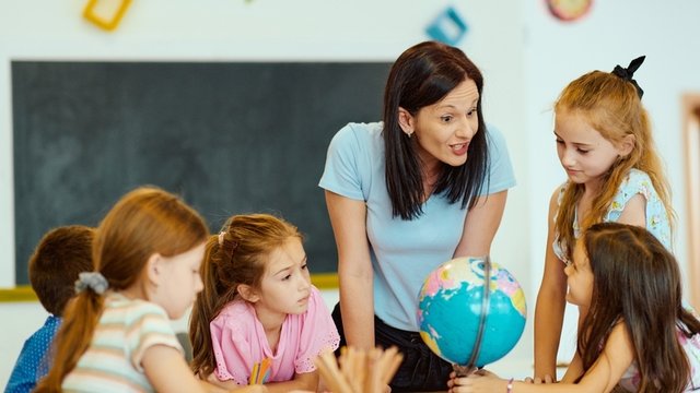Profesor de escuela primaria guiando a estudiantes curiosos alrededor del mundo durante una lección de geografía en el aula