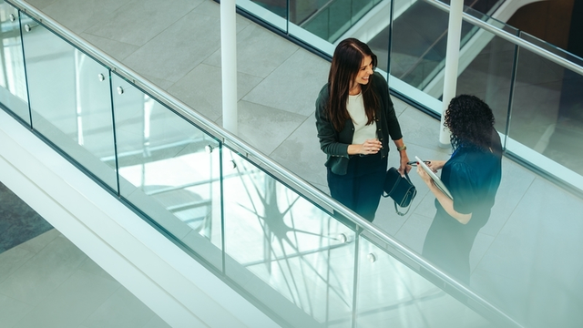 dos mujeres de negocios mantienen una conversaci&oacute;n en el pasillo