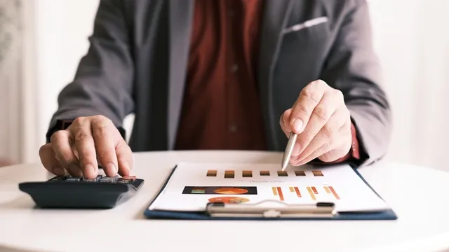 persona con chaqueta de traje revisa unos gráficos mientras hace cáculos con una calculadora