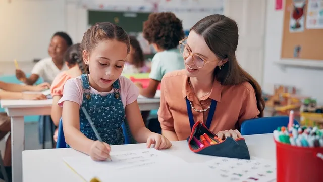 maestra ayudando a una estudiante con una tarea que está realizando en el aula