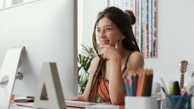 chica joven sonriente y pensativa sentada frente a un ordenador