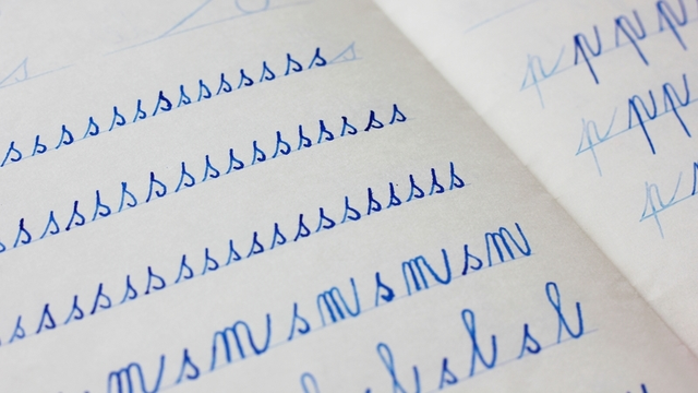 primer plano de letras azules escritas en cursiva por un ni&ntilde;o en un cuaderno de papel con l&iacute;neas