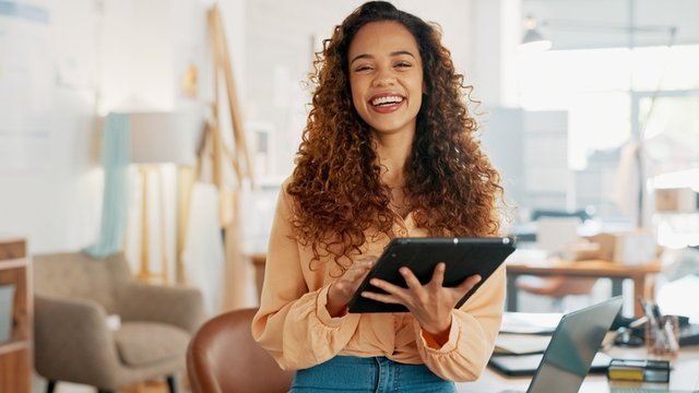 mujer sostiene una tableta y sonríe a cámara, está revisando los pedidos de su tienda online