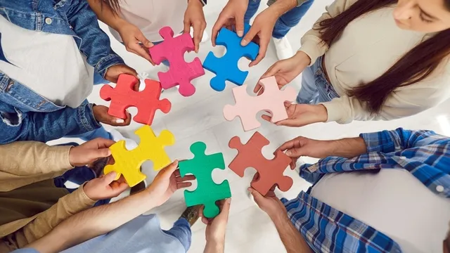 Vista superior de individuos conectando piezas de rompecabezas multicolores, representando el trabajo en equipo y la unidad