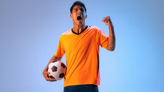 Motivated footballer wearing uniform and holding a ball