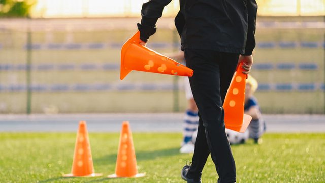 entrenador de fútbol poniendo conos sobre el terreno de juego para practicar entrenamiento físico