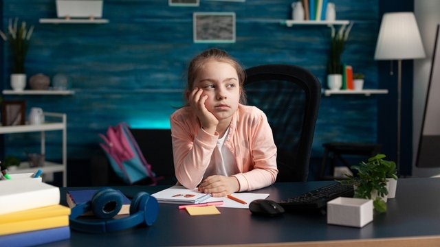 niña pensativa sentada frente a un escritorio