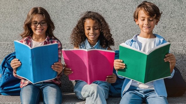 res estudiantes sentados en un banco de hormigón leen unos cuadernos
