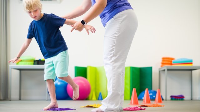 niño realiza una actividad con alfombras sensoriales texturizadas y recibe la ayuda de una persona adulta