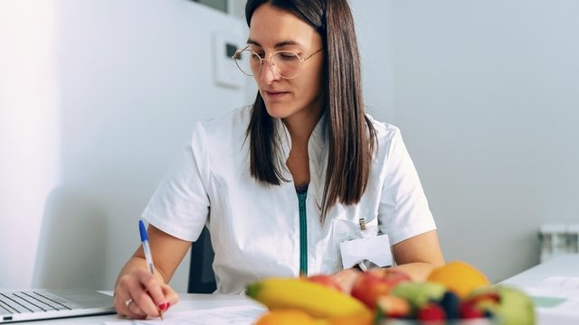 mujer trabaja con un ordenador portátil mientras toma notas en una consulta de nutrición